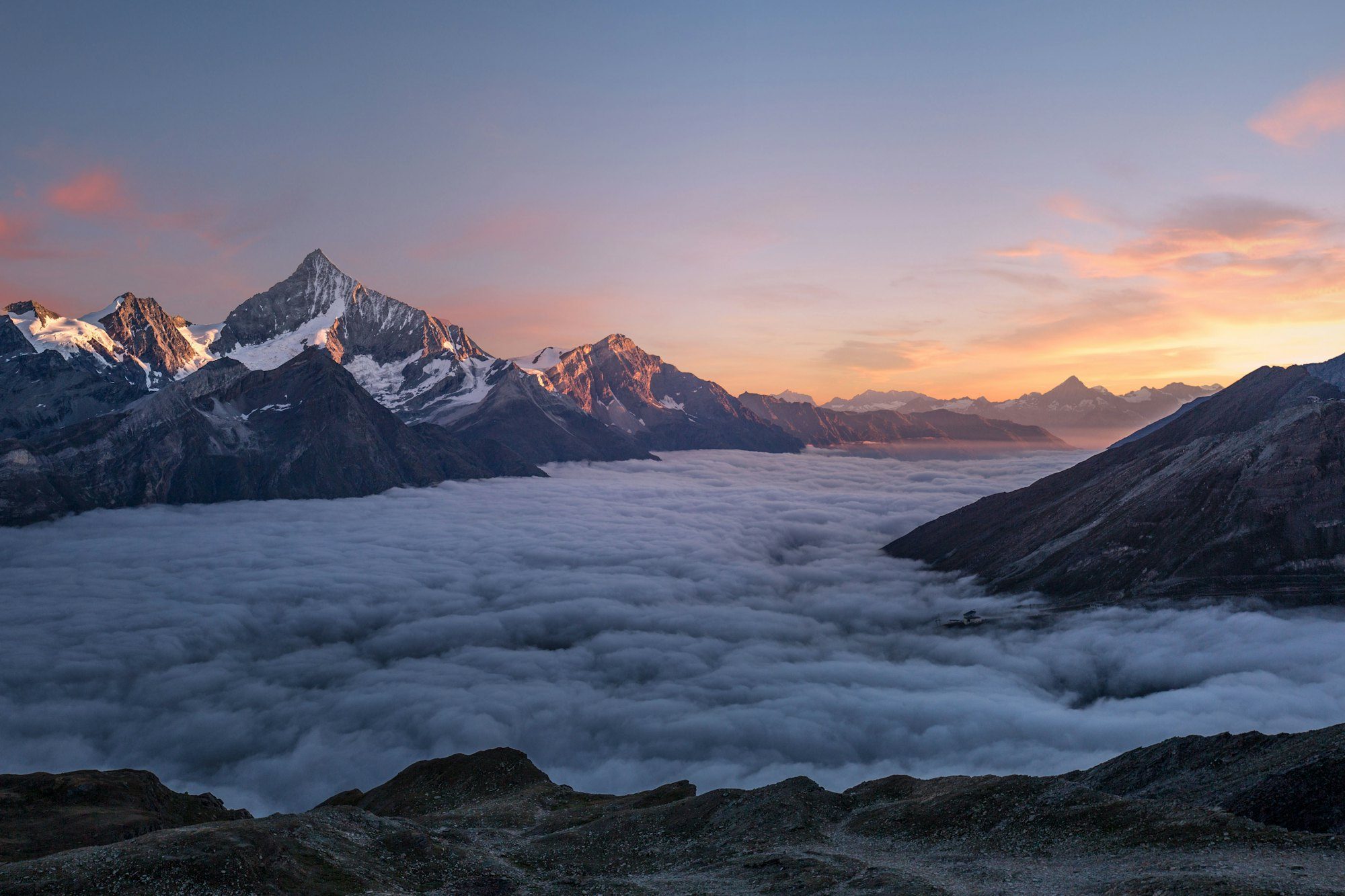 Snow peaks rising above a sea of cloud at dusk